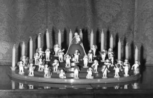 [Translate to Englisch (Intl):] Schwarz-Weiß-Aufnahme vom Engelorchester mit Madonna auf einem Engelberg. Auf den unteren Stufen die Engelmusikanten. An oberster Stelle die Madonna mit Schleier und im langen Kleid. Im Hintergrund Kerzen. 